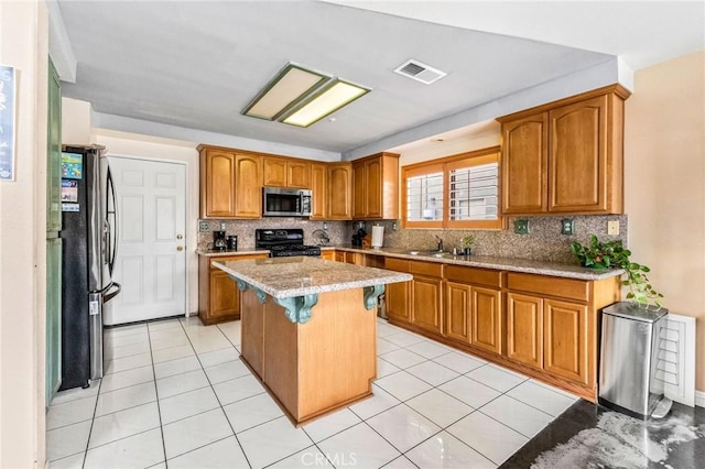 kitchen with light stone counters, light tile patterned floors, a center island, and appliances with stainless steel finishes