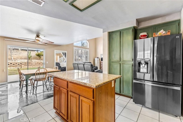 kitchen featuring fridge with ice dispenser, light tile patterned floors, light stone counters, and a kitchen island