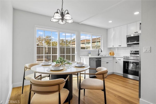 kitchen with appliances with stainless steel finishes, decorative light fixtures, white cabinetry, backsplash, and light hardwood / wood-style flooring