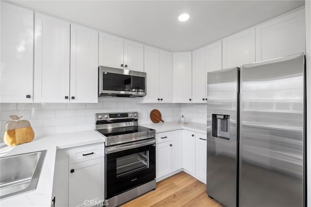 kitchen with sink, white cabinetry, stainless steel appliances, tasteful backsplash, and light hardwood / wood-style floors