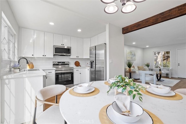 kitchen with sink, white cabinetry, beam ceiling, stainless steel appliances, and decorative backsplash