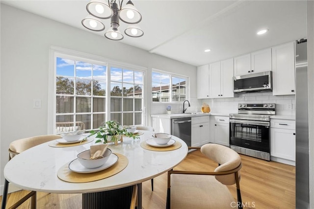 kitchen featuring white cabinetry, decorative backsplash, light wood-type flooring, and appliances with stainless steel finishes