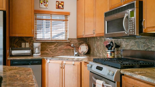 kitchen featuring tasteful backsplash, appliances with stainless steel finishes, light stone countertops, and sink