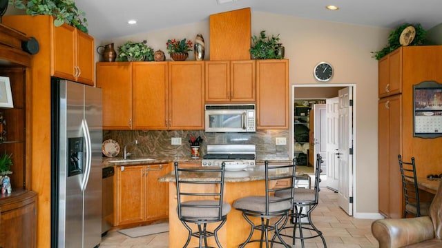 kitchen with lofted ceiling, stainless steel appliances, a center island, a kitchen bar, and decorative backsplash