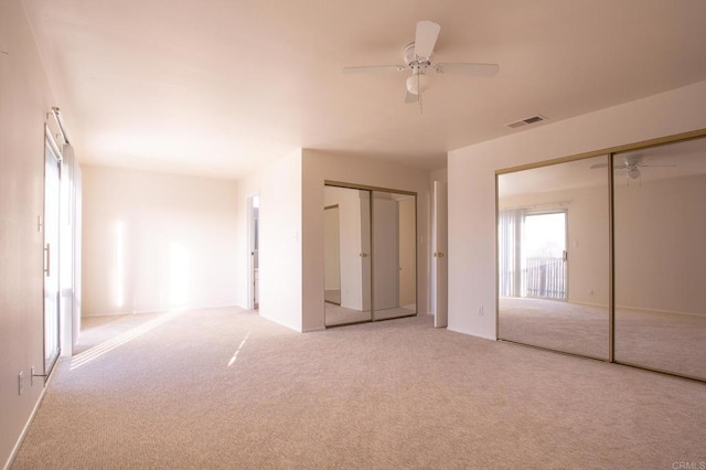 unfurnished bedroom with multiple closets, light carpet, and ceiling fan