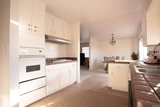 kitchen featuring white cabinetry, sink, oven, hanging light fixtures, and light carpet