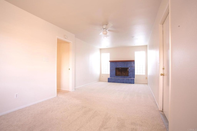 unfurnished living room with a tiled fireplace, light carpet, and ceiling fan