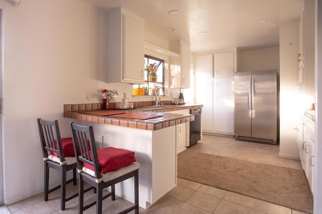 kitchen featuring sink, tile countertops, stainless steel refrigerator, dishwasher, and white cabinets