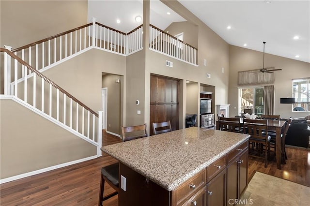 kitchen with dark hardwood / wood-style flooring, light stone countertops, a center island, and a high ceiling