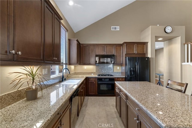 kitchen featuring sink, a breakfast bar area, backsplash, light stone counters, and black appliances