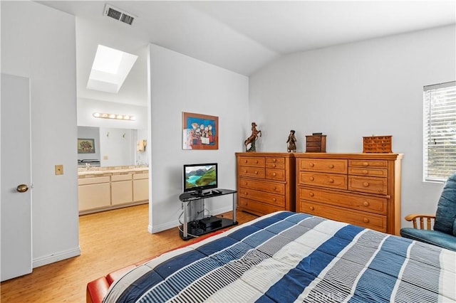 bedroom with ensuite bath, lofted ceiling with skylight, and light hardwood / wood-style floors