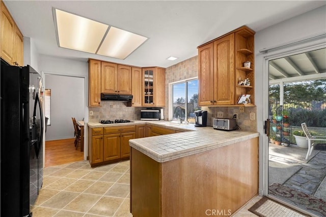 kitchen featuring sink, black appliances, tile counters, kitchen peninsula, and backsplash