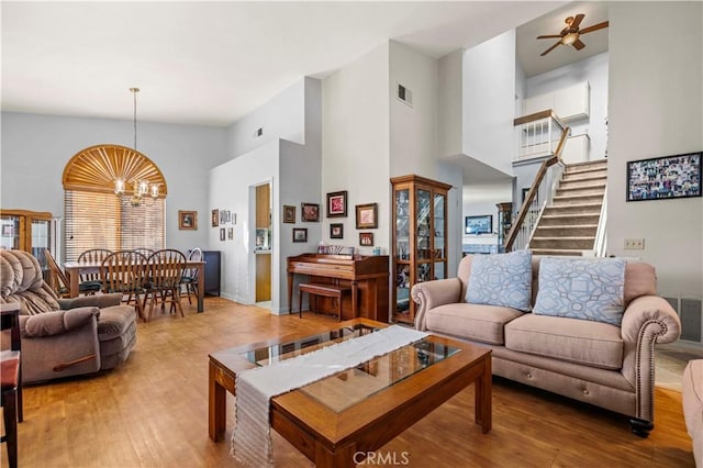 living room with a high ceiling, wood-type flooring, and ceiling fan with notable chandelier