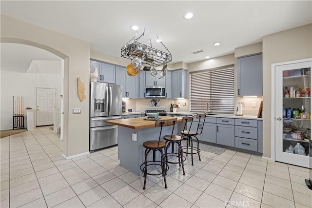 kitchen with a kitchen island, a breakfast bar, wood counters, light tile patterned floors, and stainless steel appliances