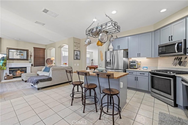 kitchen with light tile patterned floors, a breakfast bar area, stainless steel appliances, a center island, and wood counters