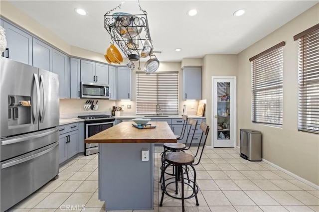 kitchen with butcher block countertops, sink, stainless steel appliances, a center island, and decorative light fixtures