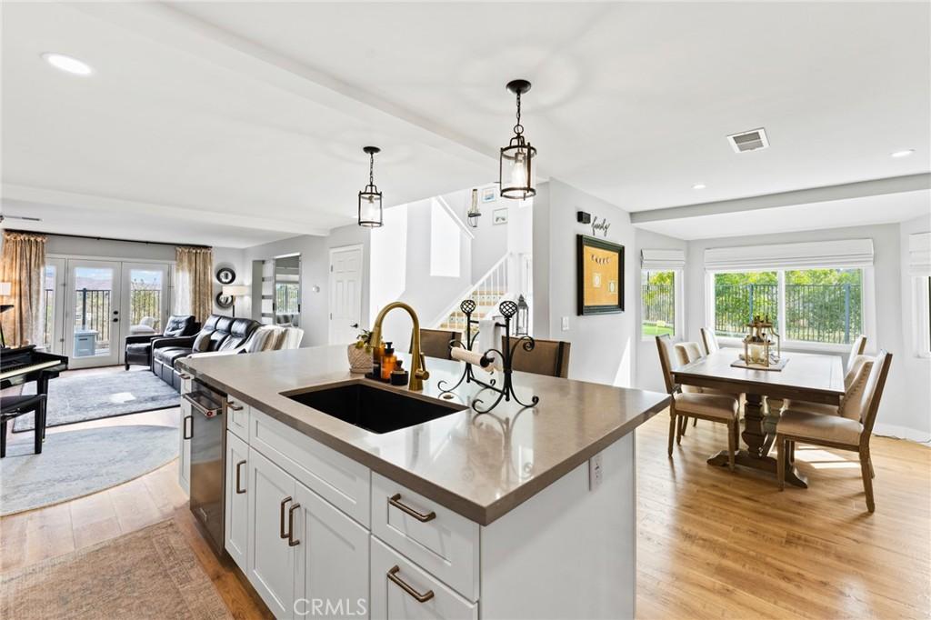 kitchen with french doors, sink, hanging light fixtures, an island with sink, and white cabinets