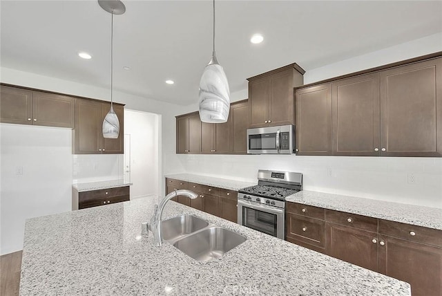 kitchen with sink, decorative light fixtures, dark brown cabinets, appliances with stainless steel finishes, and light stone countertops