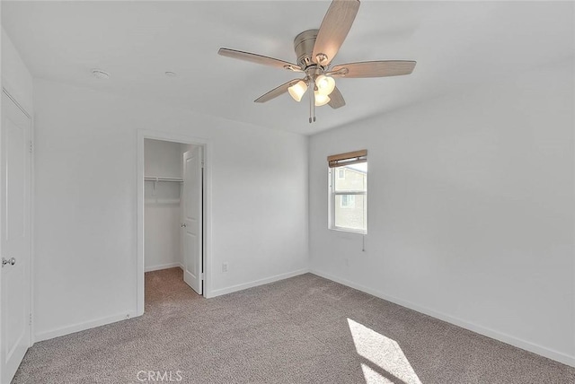 unfurnished bedroom featuring a spacious closet, light colored carpet, a closet, and ceiling fan