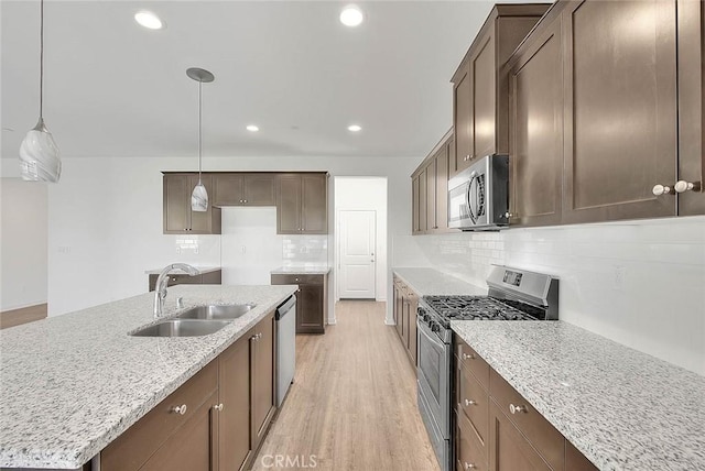 kitchen with sink, stainless steel appliances, light stone countertops, an island with sink, and decorative light fixtures