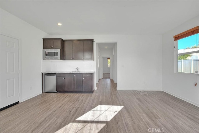 kitchen with appliances with stainless steel finishes, dark brown cabinets, sink, and light hardwood / wood-style flooring