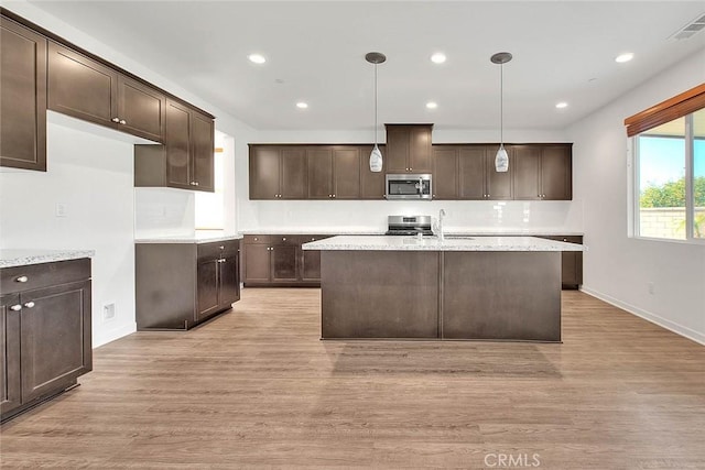 kitchen with dark brown cabinetry, appliances with stainless steel finishes, light wood-type flooring, and decorative light fixtures