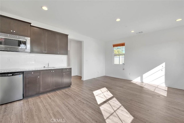 kitchen with appliances with stainless steel finishes, dark brown cabinets, light stone counters, and light hardwood / wood-style floors