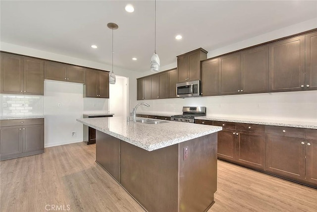 kitchen with sink, appliances with stainless steel finishes, dark brown cabinetry, decorative light fixtures, and light wood-type flooring