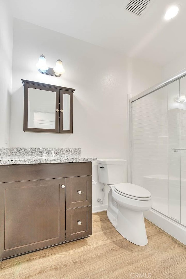 bathroom featuring vanity, wood-type flooring, a shower with shower door, and toilet