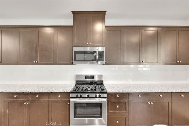 kitchen featuring light stone counters, tasteful backsplash, stainless steel appliances, and dark brown cabinetry