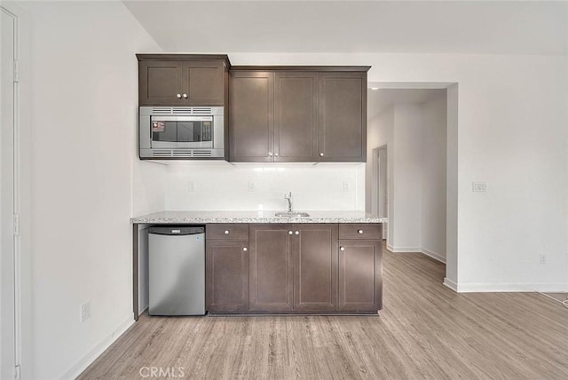 kitchen with light stone counters, dark brown cabinets, stainless steel appliances, and light hardwood / wood-style flooring