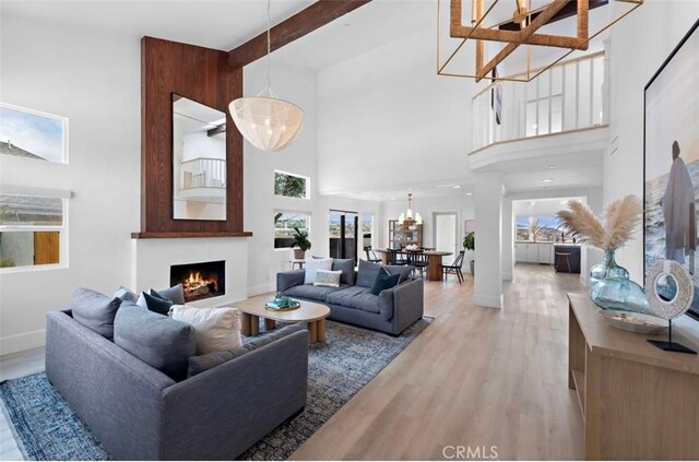 living room featuring a notable chandelier, beam ceiling, light hardwood / wood-style flooring, and a high ceiling