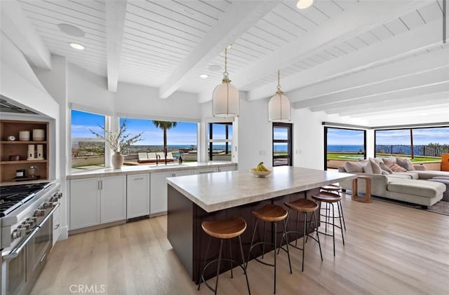 kitchen with a kitchen bar, decorative light fixtures, a kitchen island, beam ceiling, and white cabinets