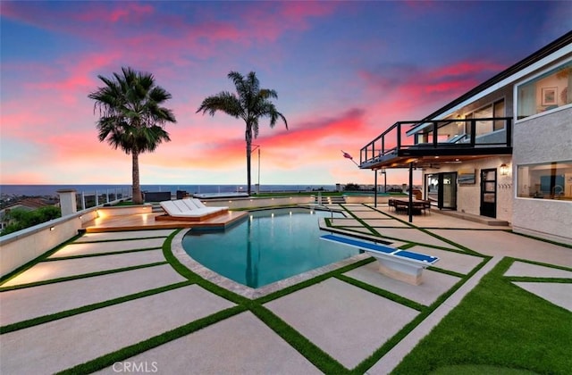 pool at dusk with a diving board and a patio area