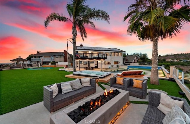 back house at dusk with a balcony, a yard, a patio, and an outdoor living space with a fire pit