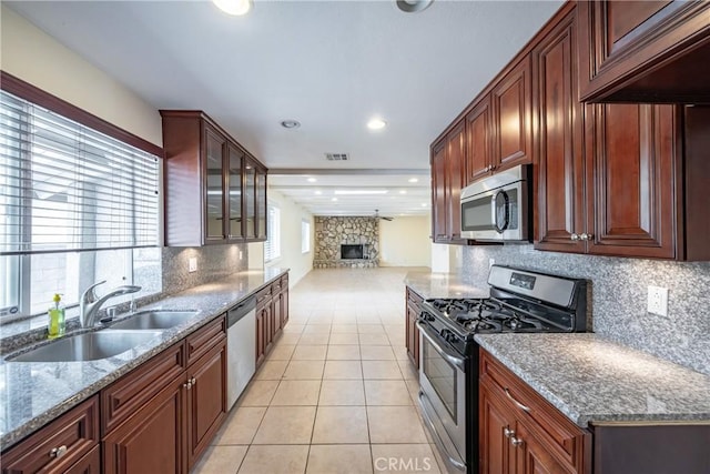 kitchen with stone counters, light tile patterned flooring, a fireplace, sink, and stainless steel appliances