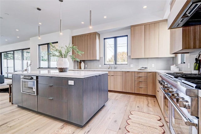 kitchen with stainless steel stove, premium range hood, hanging light fixtures, a center island, and light wood-type flooring