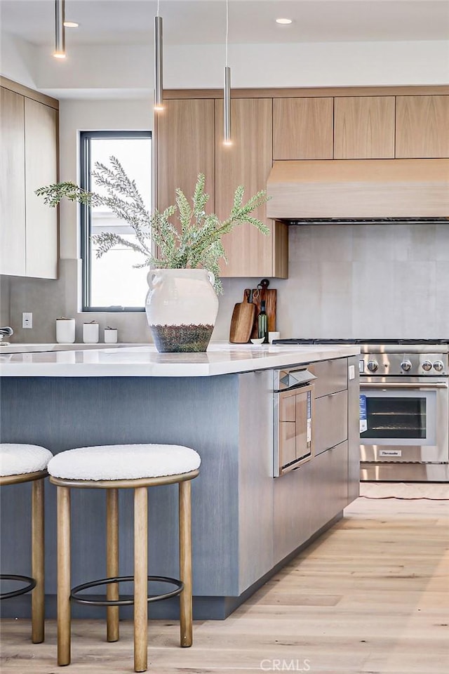 kitchen featuring light hardwood / wood-style flooring, high end range, a kitchen breakfast bar, custom exhaust hood, and oven