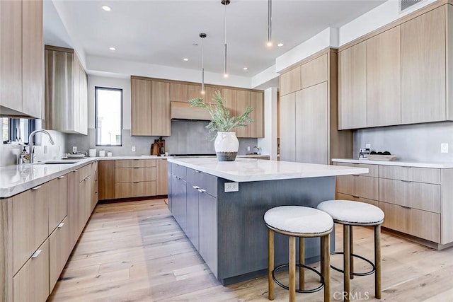 kitchen featuring pendant lighting, sink, backsplash, a large island, and light brown cabinets