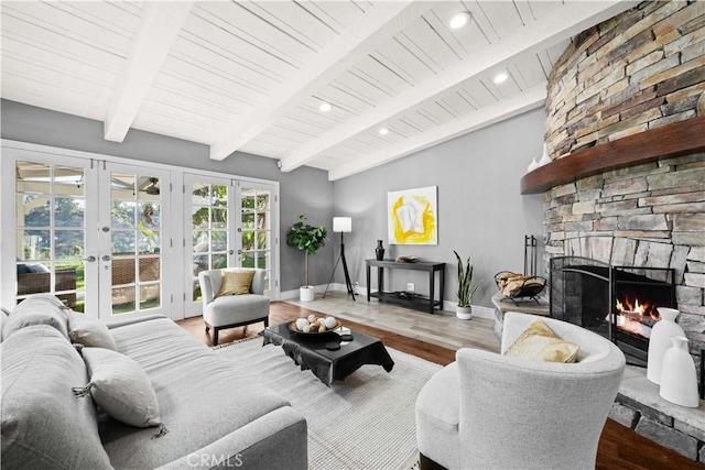 living room with hardwood / wood-style flooring, a stone fireplace, lofted ceiling with beams, and french doors