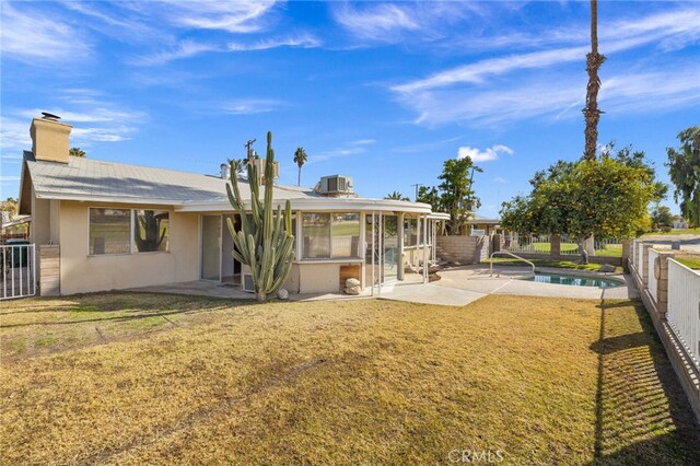 rear view of house with cooling unit, a fenced in pool, a lawn, and a patio