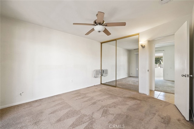 unfurnished bedroom featuring carpet floors, a closet, baseboards, ceiling fan, and a wall unit AC