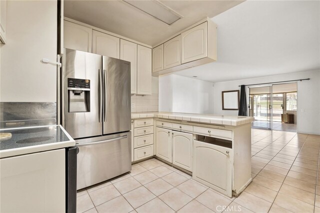 kitchen featuring stainless steel refrigerator with ice dispenser, tile countertops, light tile patterned floors, white electric stove, and kitchen peninsula