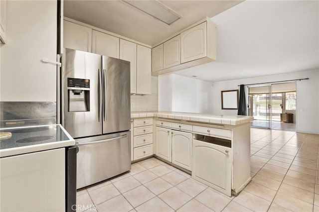 kitchen featuring a peninsula, light tile patterned flooring, stainless steel fridge, tile countertops, and range with electric cooktop