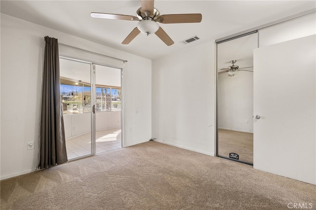 carpeted spare room featuring visible vents and a ceiling fan