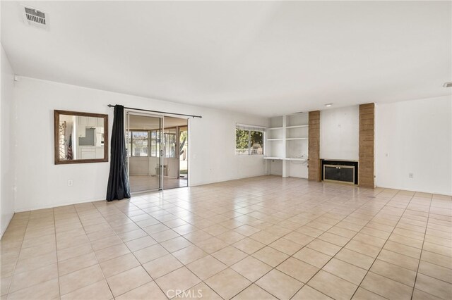 unfurnished living room with built in features, a fireplace, light tile patterned flooring, and visible vents