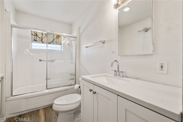 full bath featuring wood finished floors, shower / bath combination with glass door, vanity, and toilet