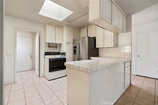 kitchen featuring range with electric stovetop, light tile patterned flooring, tile countertops, a skylight, and stainless steel fridge