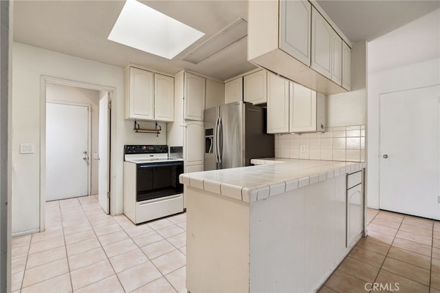 kitchen featuring stainless steel fridge, tile counters, light tile patterned floors, range with electric cooktop, and a skylight