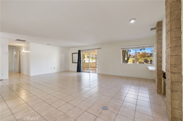 unfurnished room with a large fireplace, visible vents, and light tile patterned flooring